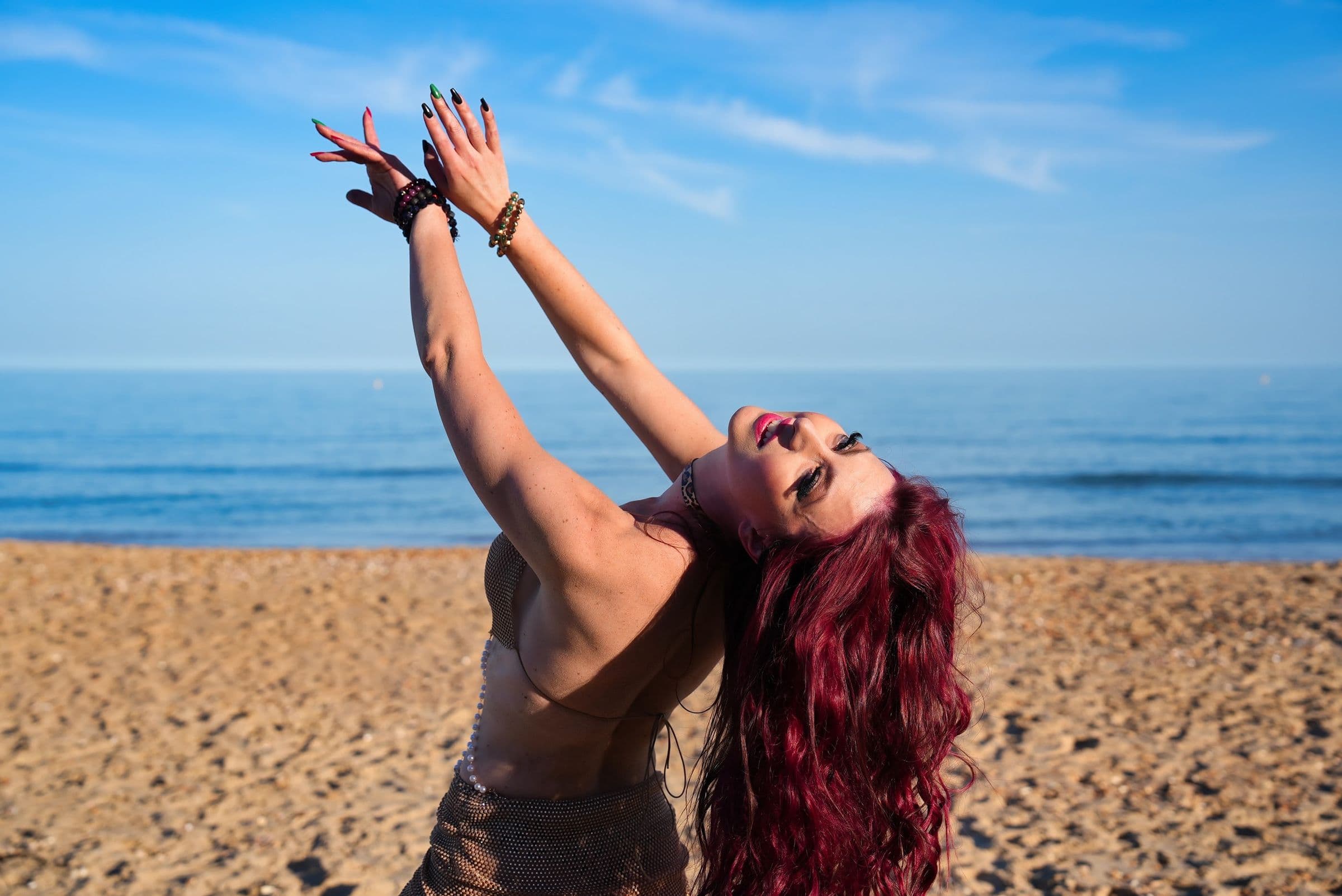 Yulia dancing on the beach, arms raised to a clear blue sky