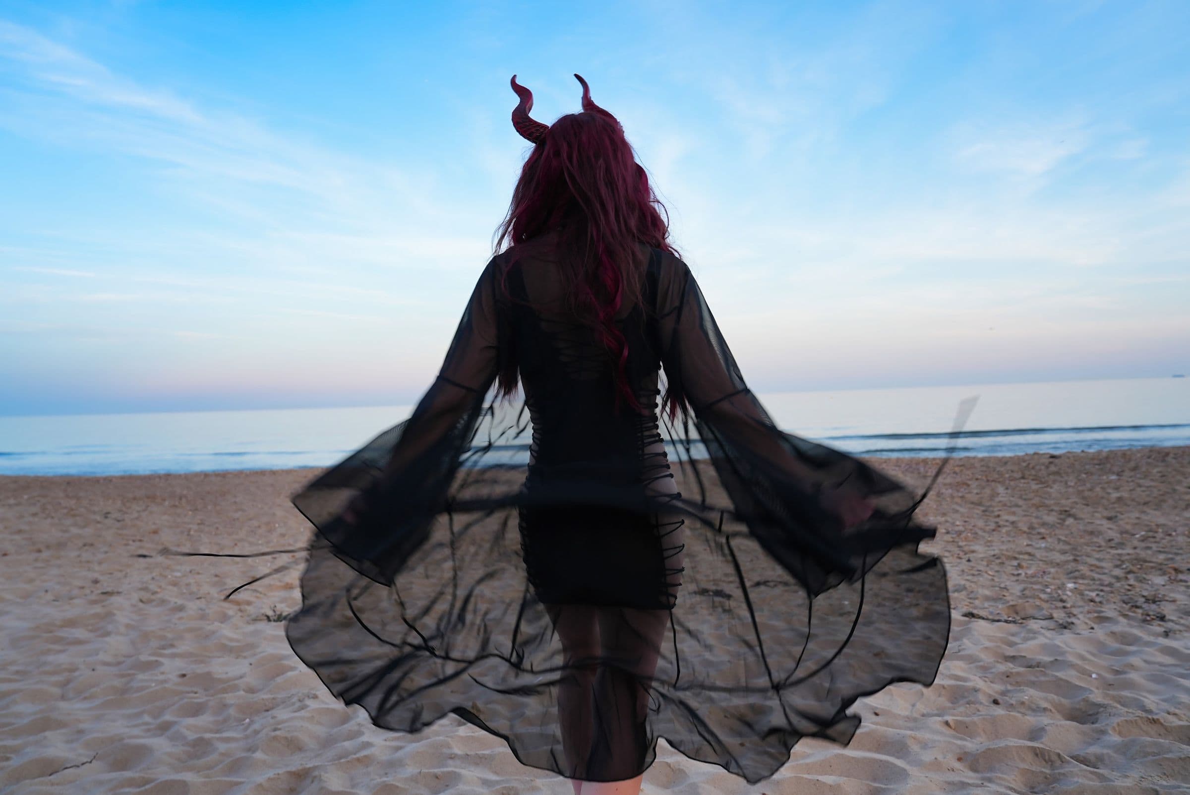 A horned figure walking towards the sea in a long sheer black cape