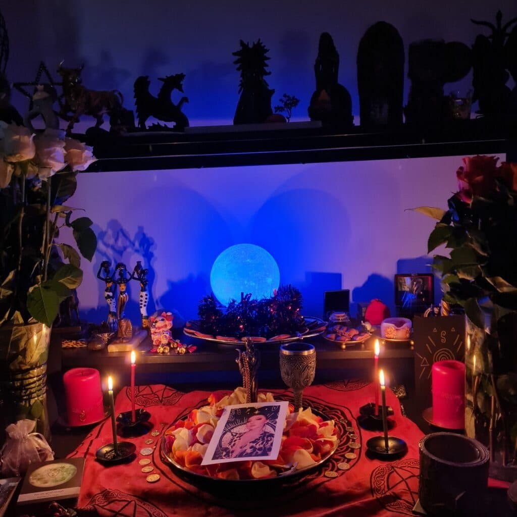 An altar in blue light with a moon lamp, candles, roses and statues