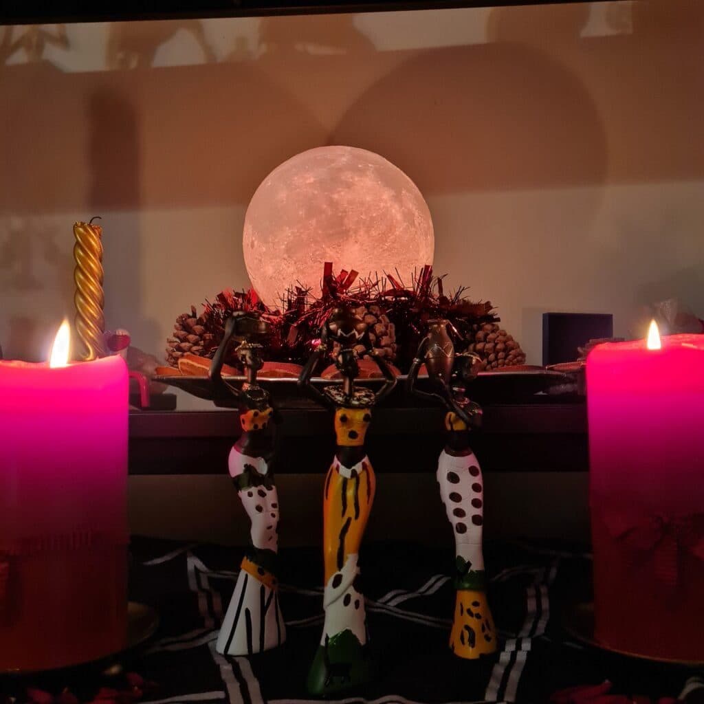 An altar lit by pink candles beneath a glowing full-moon lamp