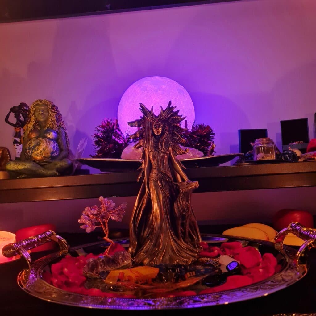 A carved goddess statue before a purple moon on a decorated altar