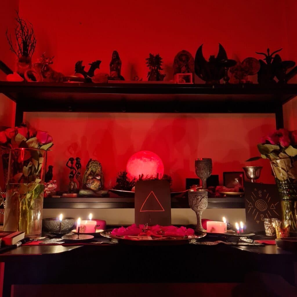 An altar bathed in red light with candles, flowers and figurines