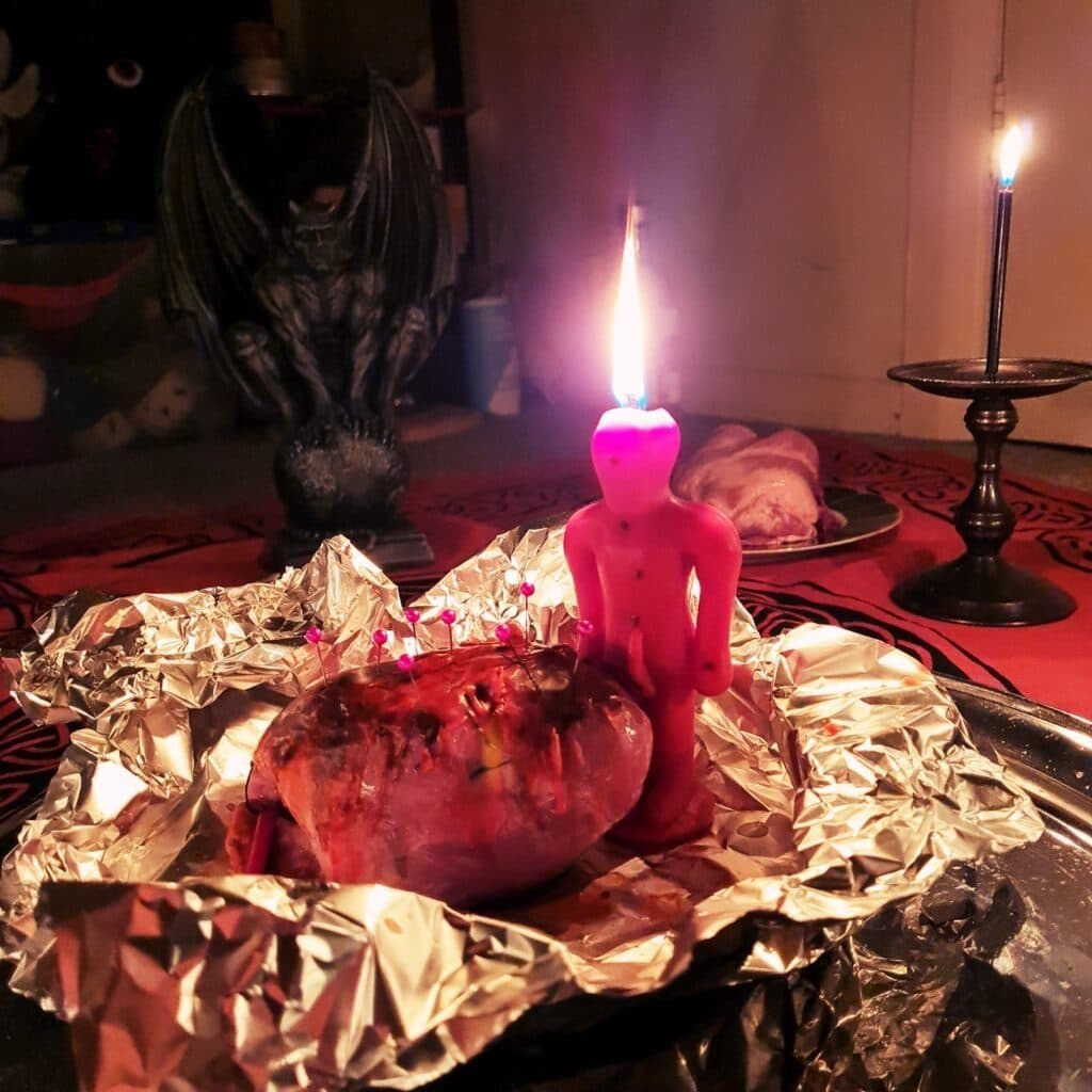 A pink figure candle burning during a spell, with a gargoyle watching