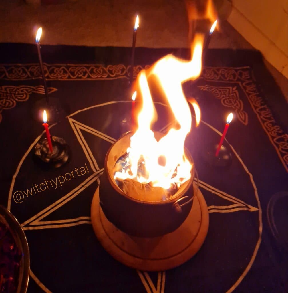 Flames rising from a cauldron on a pentacle altar cloth, candles burning around it