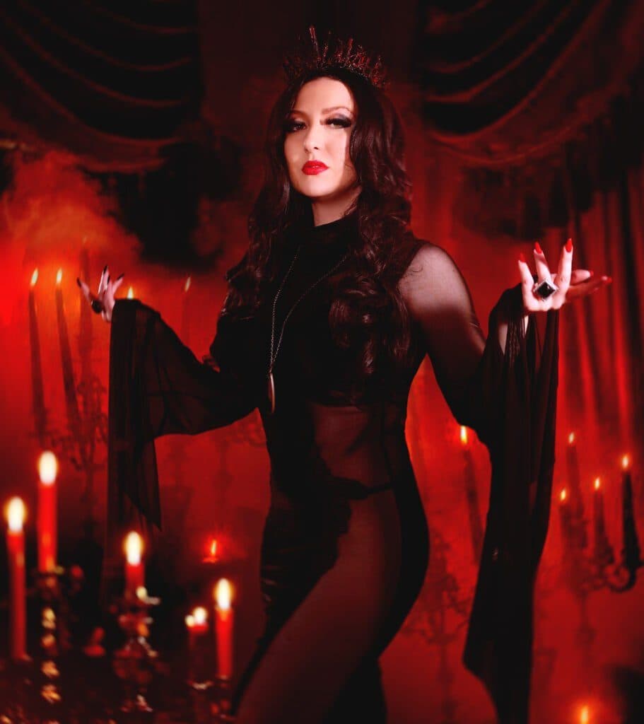 Yulia in a crown and black lace, hand raised among red candles