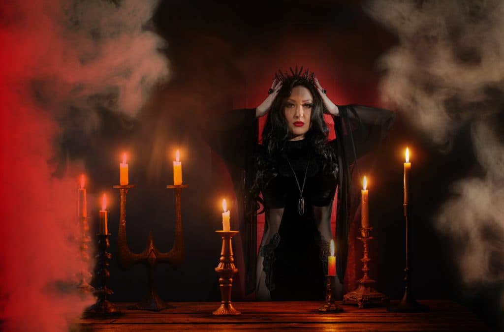 Yulia seated among lit candelabras, red smoke rising behind her